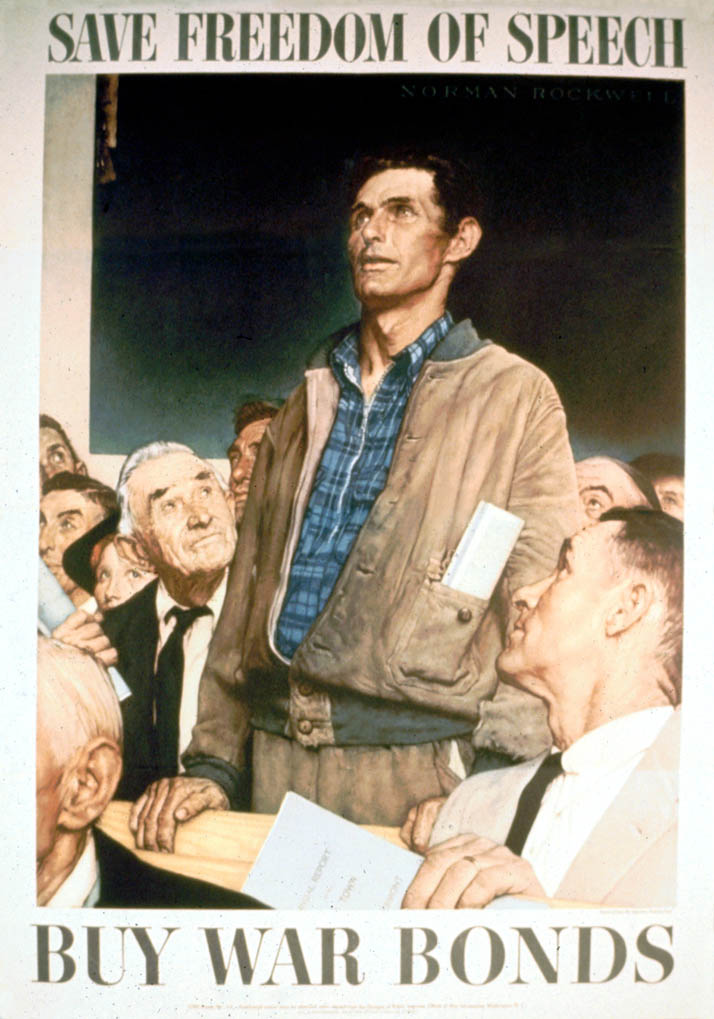 A man stands to speak at a town meeting