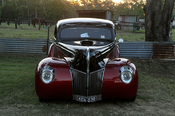 A hotrod posing in front of a rural scene as the sun sets