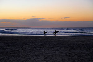 Two lone surfers at sunset