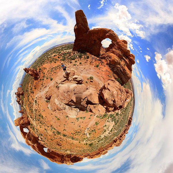 Bronwen, atop a spike of rock, takes a “little planet” of Ned standing in front of several arches