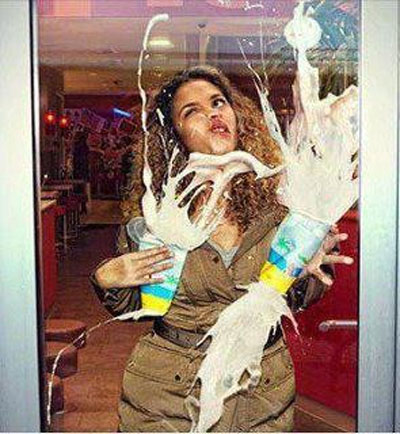 A woman runs into a door carrying two milkshakes.